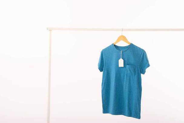 Blue t shirt with tag on hanger hanging from clothes rail with copy space on white background. Fashion, clothes, colour and fabric concept. - Foto, Imagem