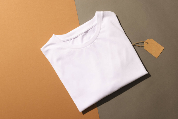Close up of folded white t shirt with tag and copy space on brown background. Fashion, clothes, colour and fabric concept. - Foto, imagen