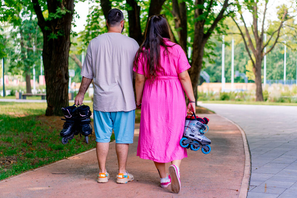 Ένα νεαρό ζευγάρι περπατά μέσα από το πάρκο, ενώ σε μια ημερομηνία κρατώντας τα χέρια και κρατώντας πατίνια στα χέρια των συν μέγεθος μοντέλα - Φωτογραφία, εικόνα