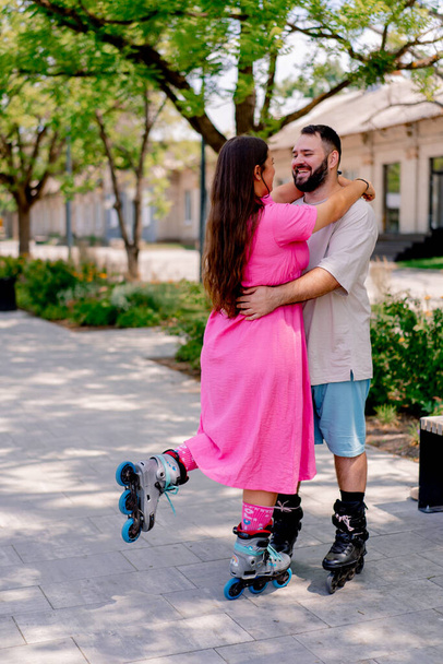 Νεαρό ζευγάρι σε rollerblades τύπος και κορίτσι αγκαλιά κατά τη διάρκεια της ημερομηνίας στο πάρκο συν τα μοντέλα μεγέθους - Φωτογραφία, εικόνα