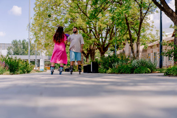 Joven pareja chico y chica patinando en verano en el parque de la ciudad mientras citas más modelos de tamaño - Foto, imagen