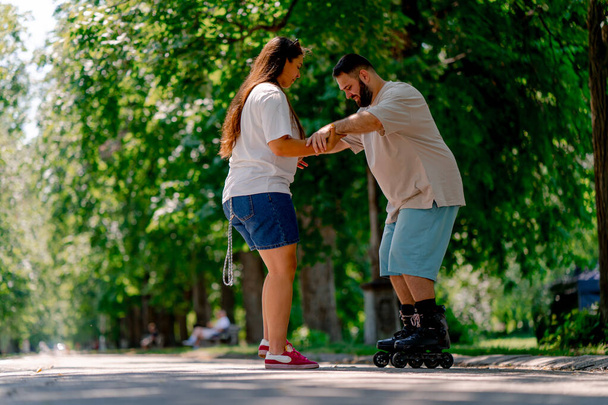 Jovem casal menina segura as mãos do cara que está patinando e ajuda-o a aprender a patinar no parque mais modelos de tamanho - Foto, Imagem