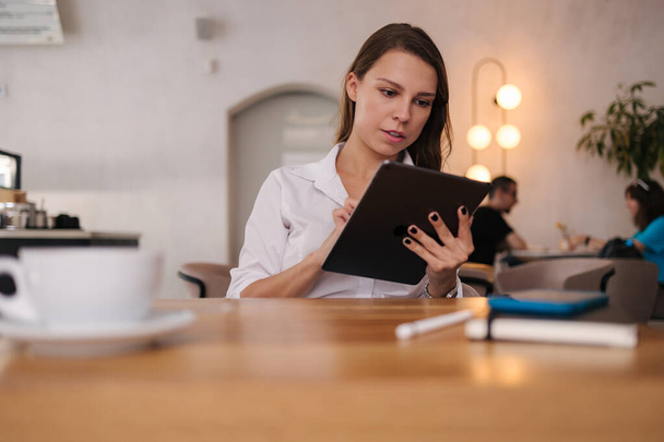 Kafede dijital tablet kullanan serbest çalışan bir kadın. Genç işletme müdürü iş arasında kahve içer. Yüksek kalite fotoğraf - Fotoğraf, Görsel