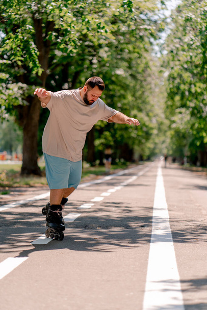 Young guy with beard learns to rollerblade in a city park concept of wanting to learn new things and body positivity - Photo, Image