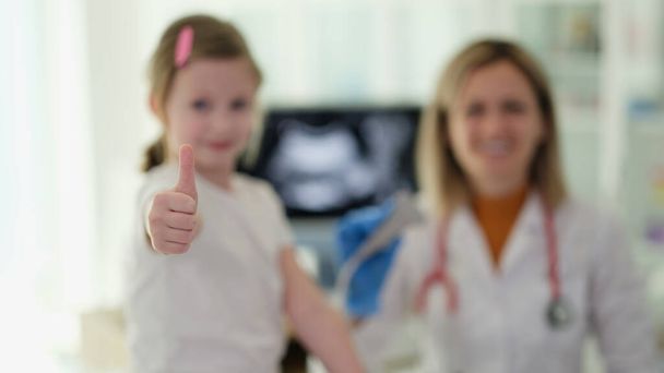 小さな女の子は医師の診察で親指でジェスチャーをする. 質の高い小児科医のサービス - 写真・画像