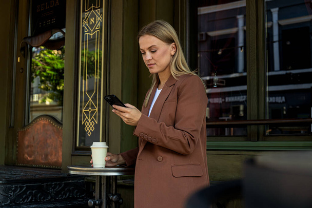 Mulher de negócios com smartphone e copo de papel em mãos ao ar livre - Foto, Imagem