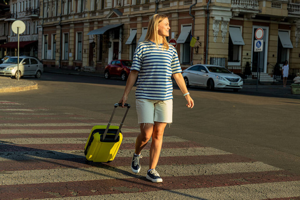 Smiling young woman with suitcase in the city - Photo, Image