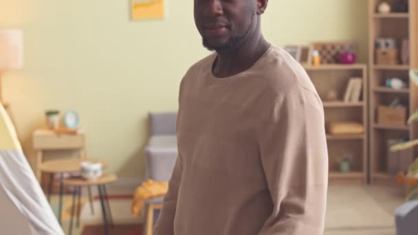 Приглушений портрет молодого чорного чоловіка, який позує зі складеними руками, стоячи в затишній вітальні вдома - Кадри, відео