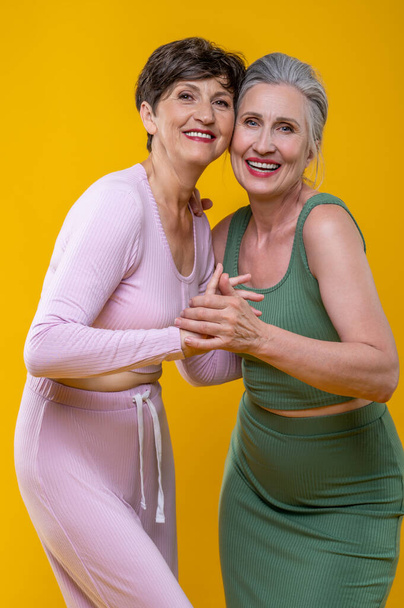 Women. Active senior women standing close and smiling happily - Foto, afbeelding