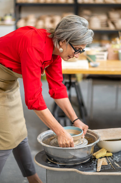 Ceramista donna anziana di talento che prende piatto finito dalla ruota della ceramica, rendendo terracotta. - Foto, immagini