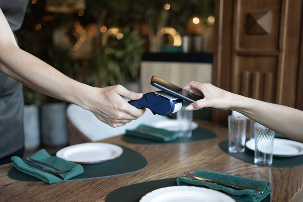カフェでスマートフォンを通して法案を手渡す. 無接触技術を使用して携帯電話を介して支払う幸せな顧客. ワイヤレスバンキング決済コンセプト。 NFC技術について。 前景に焦点を当てる. - 写真・画像