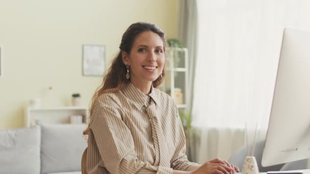 Portrait taille haute de belle jeune femme d'affaires brune souriant à la caméra tout en travaillant sur ordinateur au bureau à partir de lumineux bureau à domicile spacieux - Séquence, vidéo