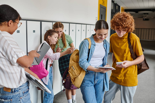 adolescentes estudantes com dispositivos no corredor da escola, mulher afro-americana perto de escolares, mulher negra - Foto, Imagem
