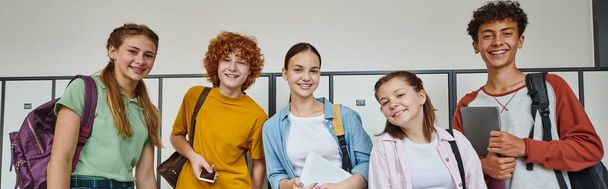 banner, cheerful teenage students holding devices and looking at camera in school hallway, friends - Photo, Image