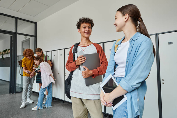 счастливые школьники, держащие устройства в коридоре, возвращающиеся в школу концепция, улыбка, студенты и технологии - Фото, изображение