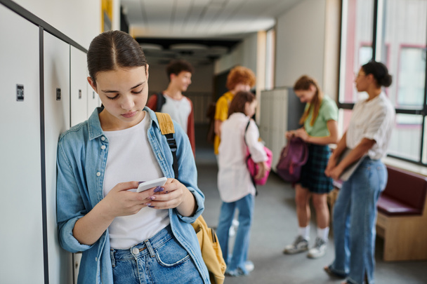 mensajes de texto de chicas adolescentes en el teléfono inteligente en el pasillo de la escuela, estudiantes y profesores en un fondo borroso - Foto, imagen