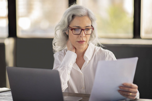 Entrepreneurship, Business Paperwork. Manager Lady Reading Bills And Reports Sitting At Table Near Laptop, Working With Papers In Office Interior, Wearing Glasses. Career Concept - Foto, immagini