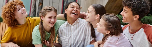 pancarta, mujer afroamericana feliz abrazándose con estudiantes adolescentes, diversidad, maestra, sonrisa - Foto, Imagen