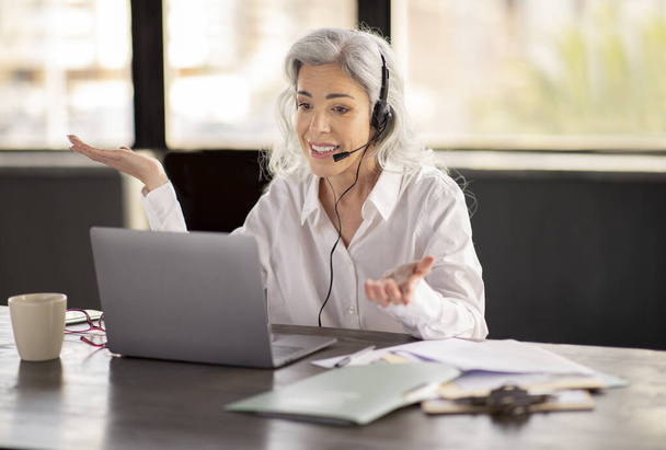 Müşteri desteği. Telsiz operatörü iş kadını kulaklık takıyor ve işyerindeki bilgisayarla konuşuyor, müşterilere çevrimiçi yardım ediyor, müşteri sorunlarını iletişim yoluyla çözüyor. - Fotoğraf, Görsel
