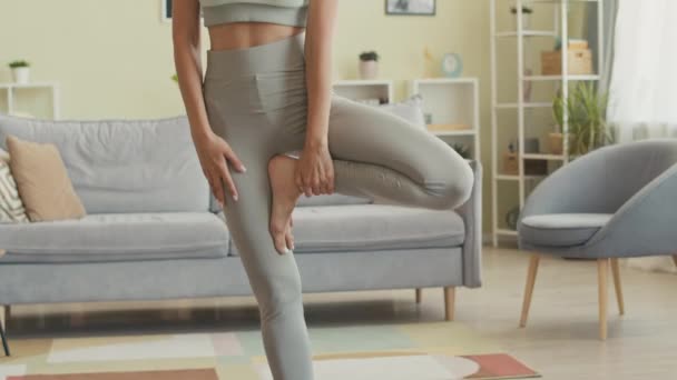 Приглушений знімок молодої стрункої жінки, що стоїть в одній нозі йога позує, зберігаючи баланс, практикуючи йогу вдома поодинці - Кадри, відео