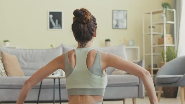 Вид на молодую брюнетку с татуировкой иероглифа на шее, практикующую йогу в спокойной домашней обстановке - Кадры, видео