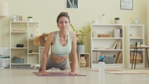 Jovem mulher caucasiana em activewear apertado fazendo postura de cão virada para cima enquanto pratica asanas de ioga no tapete em casa - Filmagem, Vídeo