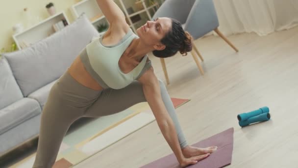 Ручной снимок молодой гибкой женщины в обтягивающей одежде, практикующей йогу, позирующей на коврике в светлой просторной гостиной - Кадры, видео