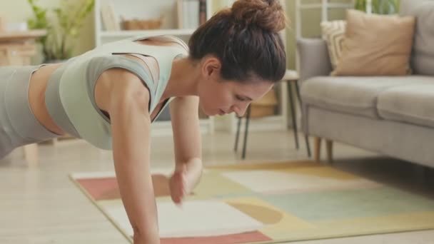 Młoda sportowa kobieta robi ćwiczenia na desce, aby wzmocnić ramiona i rdzeń podczas treningu na macie w domu - Materiał filmowy, wideo