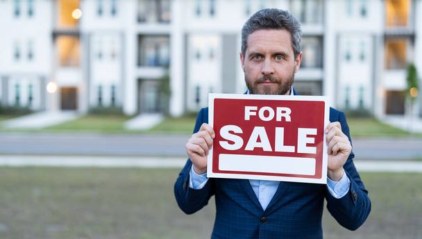 photo of salesman with for sale board, copy space banner. sale property by salesman. man salesman hold board for sale property. sale property by salesman outdoor. - Foto, afbeelding