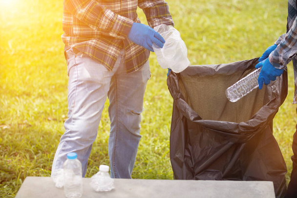 Deux employés utilisent des sacs poubelles noirs pour recueillir les bouteilles en plastique et les déchets recyclables de la pelouse et des trottoirs aux fins de recyclage. Concept de tri des déchets plastiques pour recyclage - Photo, image