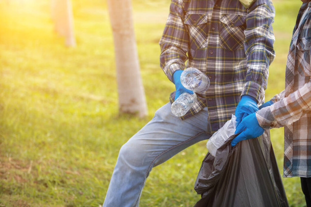 Männer sammeln Plastikflaschen auf Rasenflächen und Gehwegen im Park und legen sie in Säcke, um sie sauber zu halten. Sie können auch Plastikflaschen für das Recycling sammeln. Reduzierung von Umweltproblemen durch Recycling - Foto, Bild
