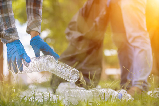мужчины собирают пластиковые бутылки на газонах и дорожках в парке и положить их в мешки, чтобы помочь сохранить их чистыми Они также могут собирать пластиковые бутылки для переработки. сокращение экологических проблем за счет переработки - Фото, изображение