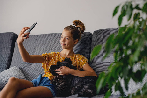 Έννοια φιλίας. έφηβος κορίτσι καυκάσιος λαμβάνοντας selfie με το σκυλί της στο σπίτι - Φωτογραφία, εικόνα
