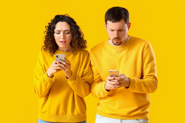黄色の背景に携帯電話を使用して若いカップルをアップセット - 写真・画像