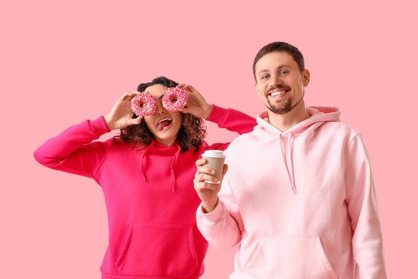 Молодая пара с вкусными пончиками и чашкой кофе на розовом фоне - Фото, изображение