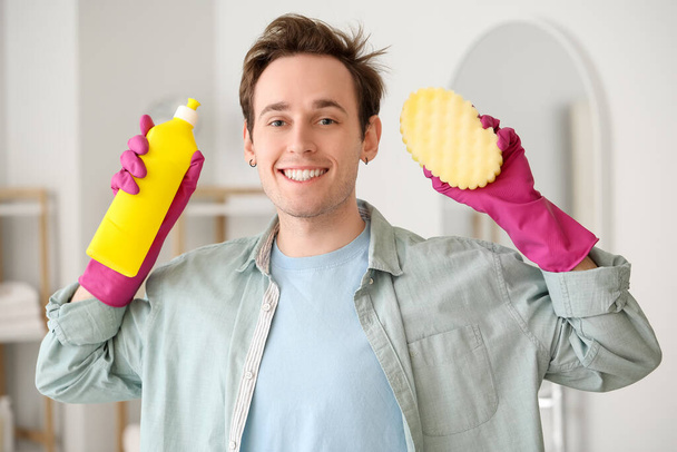 Молодой человек с чистящими средствами в ванной комнате - Фото, изображение