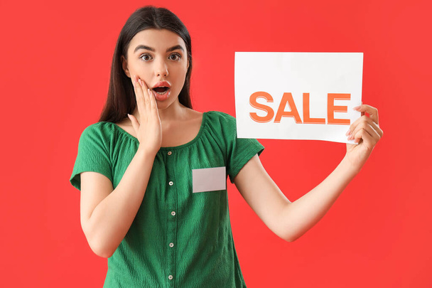 Shocked female seller with sale sign on red background - Photo, image