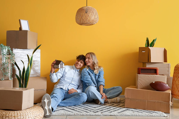 Ευτυχισμένο νεαρό ζευγάρι με σπίτι μοντέλο κάθεται στο δωμάτιο την ημέρα που κινείται - Φωτογραφία, εικόνα