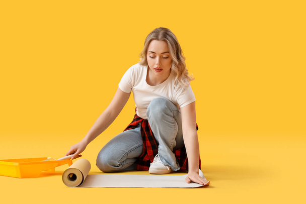 Молода жінка склеює шпалери на жовтому фоні - Фото, зображення