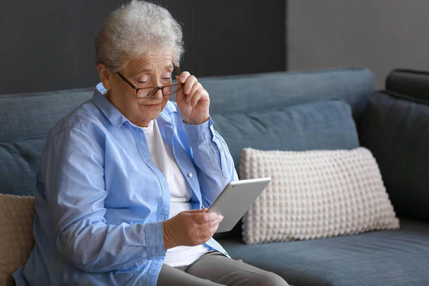 Idősebb nő szemüvegben, aki otthon táblagépet használ - Fotó, kép