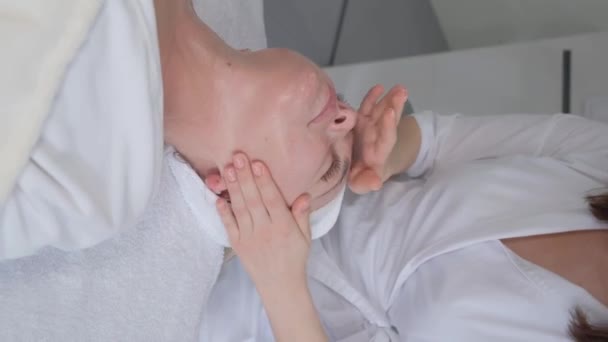 Vertical video. A beautician pleasantly massages a womans face. Anti-aging facial massage.  - Felvétel, videó