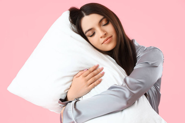 Young woman in pajamas with pillow on pink background - Photo, Image