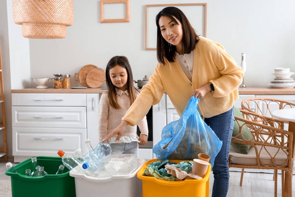 aziatische moeder met haar kleine dochter sorteren vuilnis met recycle bakken in keuken - Foto, afbeelding