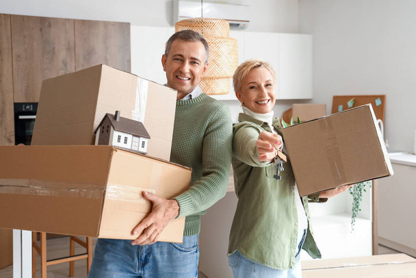 Couple d'âge mûr avec des boîtes en carton et des clés de leur nouvel appartement dans la cuisine le jour du déménagement - Photo, image
