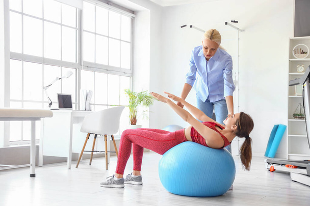 Young woman training with female physiotherapist on fitball in rehabilitation center - Photo, Image