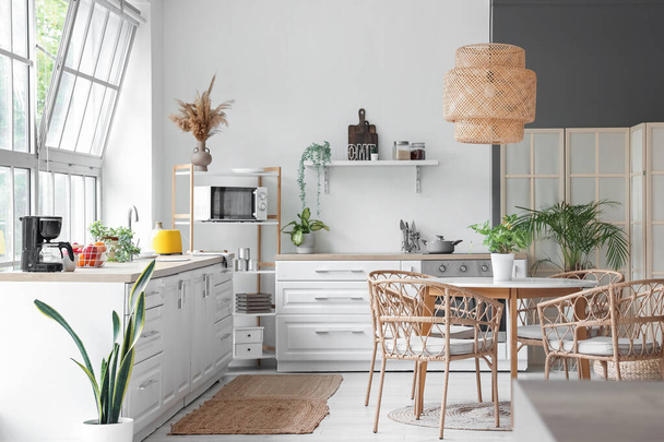Interieur van lichte keuken met witte toonbanken, eettafel en groot raam - Foto, afbeelding