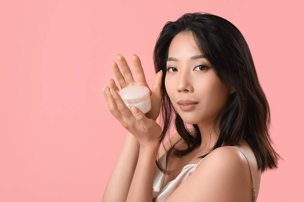 Beautiful young Asian woman with facial cream on pink background - Photo, Image