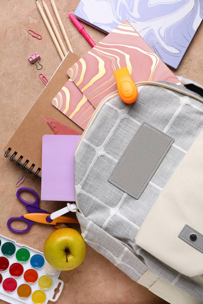 Grijze schoolrugzak met notitieboekjes, appel en aquarellen op beige grunge achtergrond - Foto, afbeelding