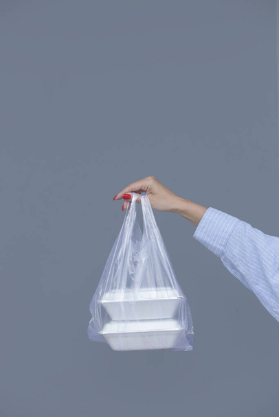 Manos de mujer sosteniendo bolsa de plástico de PVC con cajas de almuerzo de espuma para llevar. Recipientes de alimentos de un solo uso, concepto de donación. - Foto, imagen