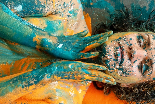 Портрет и туловище сексуальной молодой обнаженной женщины, руки которой покрывают грудь бирюзово-зеленым и оранжевым цветом. Творческая выразительная абстрактная живопись тела, копировальное пространство - Фото, изображение